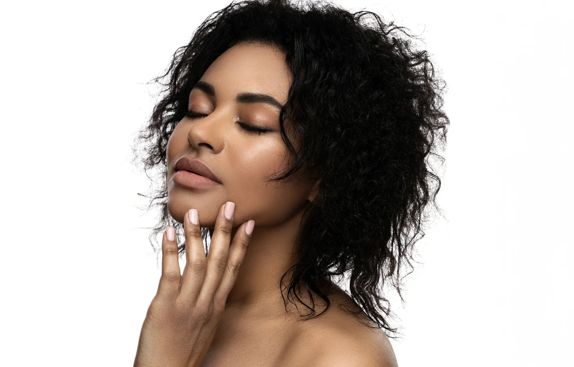Woman with curly hair gently touching her face.