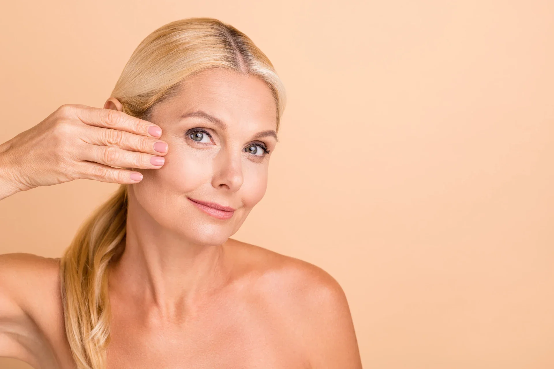 Woman holding a clear facial treatment patch against her cheek.