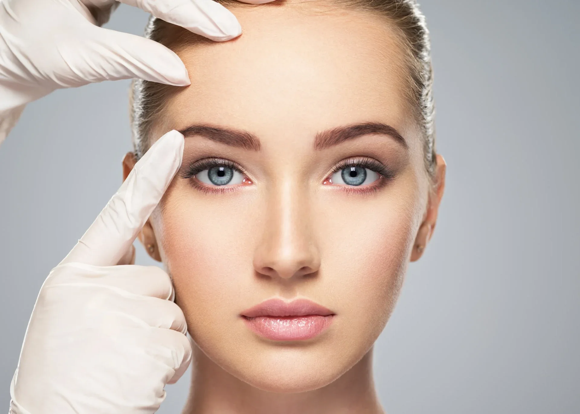 Gloved hands examining a woman’s forehead.