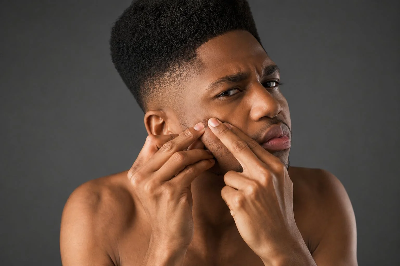 Man examining a blemish on his cheek.